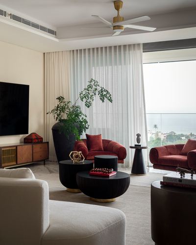 Living room with rust velvet sofas, boucle chair, black ribbed tables, sea view through sheer curtains