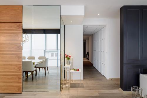Bright foyer with mirrored sliding door reflecting dining room, wood-slat corridor beyond
