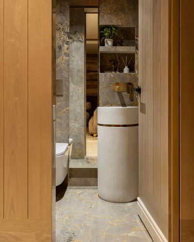 Bathroom seen through wooden door with veined stone walls and fluted pedestal sink