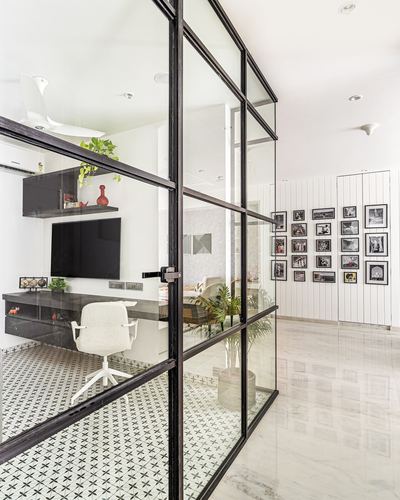 Black-framed glass partition separates a study with patterned tile floor from a marble corridor with a photo gallery wall.