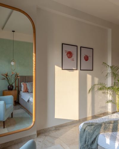 Sunlit bedroom corner with arched wooden mirror reflecting a green-walled room and framed red-toned prints