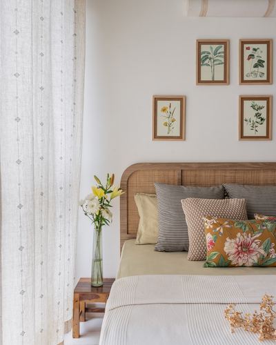 Bed with curved cane headboard, patterned cushions, and botanical prints beside sheer curtain