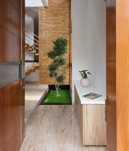 Entry foyer with wooden door, indoor tree in sunken planter, and wood console table
