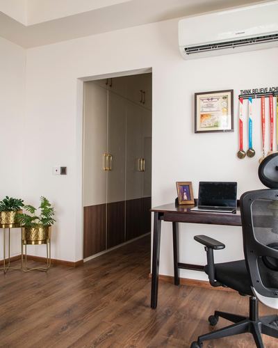 Home study nook with wooden desk, black chair, wardrobe alcove and medals rack on wall