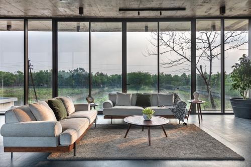 Living room with two gray sofas facing floor-to-ceiling glass walls overlooking green landscape