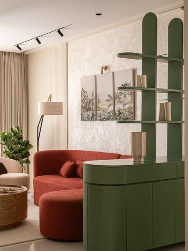Living room corner with curved terracotta sofa, green arched shelf-cabinet, and framed botanical triptych