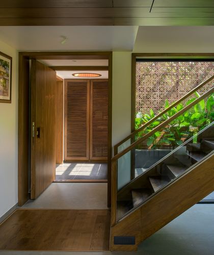 Entry foyer with wood pivot door, louvered closets, staircase, and jali screen view to garden