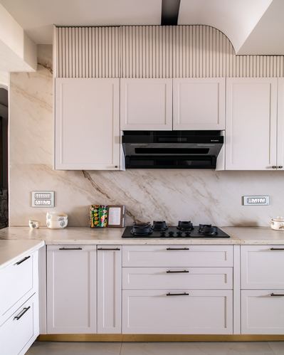White shaker kitchen with marble backsplash, black hob, and fluted curved hood panel