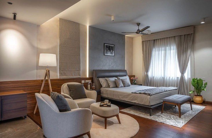 Neutral master bedroom with grey leather bed, seating nook, and backlit textured wall panel