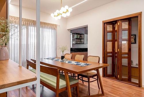 Wooden dining table with cane chairs, sphere chandelier, and cane folding door in warm-toned room