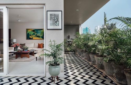 Terrace with black and white chevron floor and potted palms beside a living room seen through glass doors