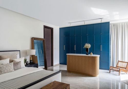 Bedroom with deep blue paneled wardrobes, fluted wood dresser, and floor mirror by bed