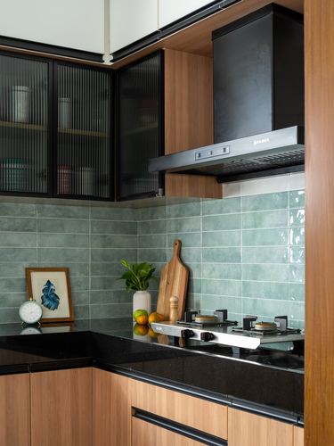 Corner of a modern kitchen with black hob, wooden cabinets and green tiled backsplash