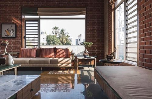 Sunlit living room with exposed brick walls, striped cushions, bonsai, and patterned stone floor