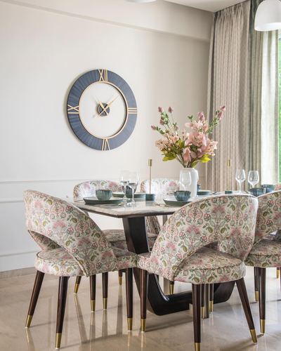 Dining table with floral chairs, marble top, and large wall clock on beige wall