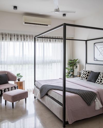 Bedroom with black metal four-poster bed, blush pink linens, and sheer curtained window