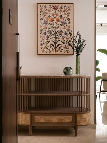 Curved wooden console with cane drawer under a floral artwork in a foyer
