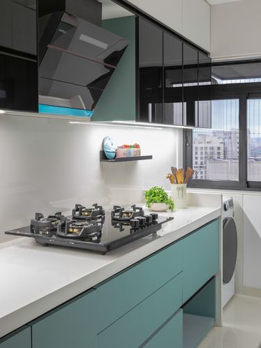 Modern kitchen with teal cabinetry, black hob, glass chimney hood, and city-view window