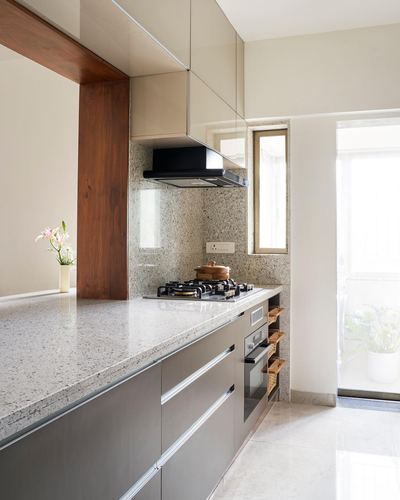 Modern galley kitchen with granite counters, grey cabinetry, and a wooden ceiling beam near a bright doorway