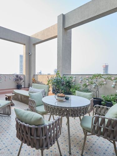 Terrace seating area with woven rope chairs, round table, and patterned tile floor overlooking Mumbai skyline