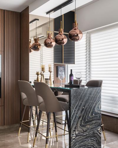 Bar counter with copper pendant lights, marble cladding, and cane-backed stools near mirrored wall