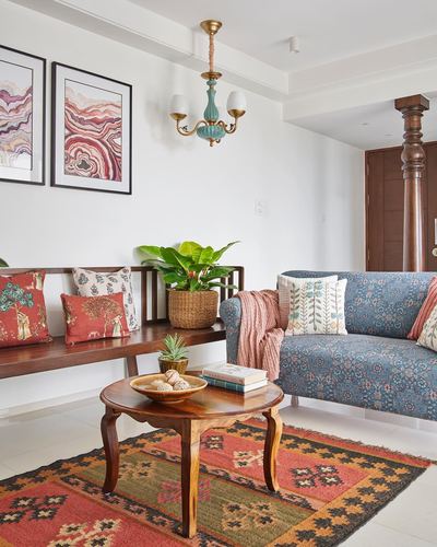 Living room with wooden bench, printed sofa, kilim rug, and blue-glass chandelier