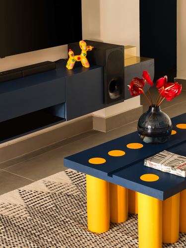 Navy TV console with balloon dog figurine beside a mustard-legged navy coffee table with red flowers