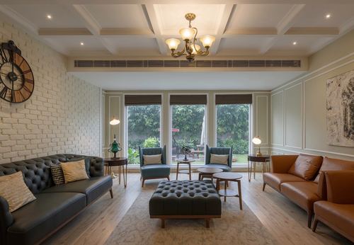 Living room with tufted sofas, coffered ceiling, brass chandelier, and garden view through large windows