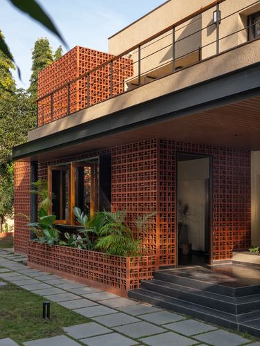 Corner view of a house with a perforated terracotta brick jali screen, steel overhang, and stone path