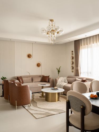 Beige living and dining space with brass chandelier, leather armchairs, and round marble-look coffee table