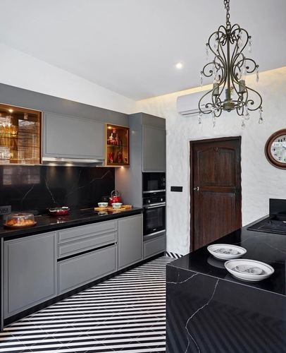 Grey kitchen with black stone counters, striped floor, wooden door and ornate pendant light