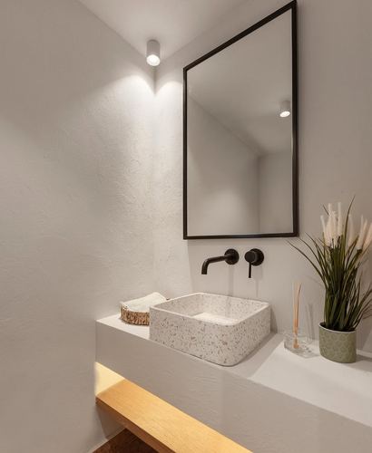 Bathroom corner with terrazzo vessel sink, black-framed mirror, and floating plaster vanity with wood underside.