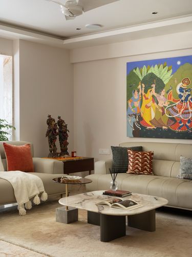 Neutral toned living room with beige sofas, marble coffee table and vibrant figurative painting on wall