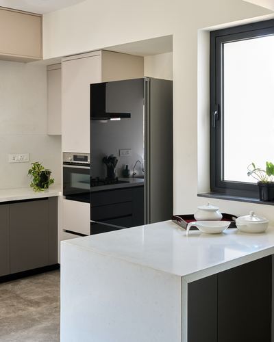 Minimalist kitchen with white waterfall island, dark cabinetry, black fridge, and window with potted plant