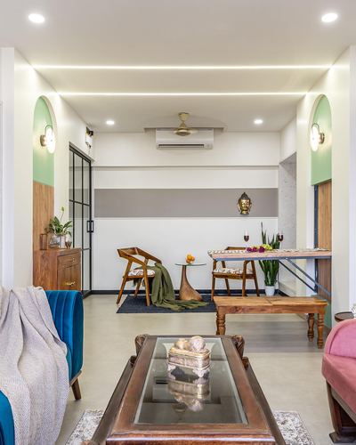 Living and dining area with teal sofa, wooden furniture, and arched green niches under cove lighting