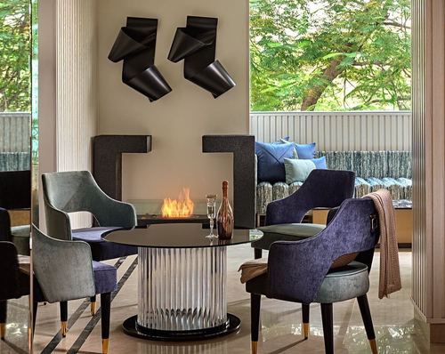 Round glass dining table with velvet chairs before a black stone fireplace and sculptural wall art