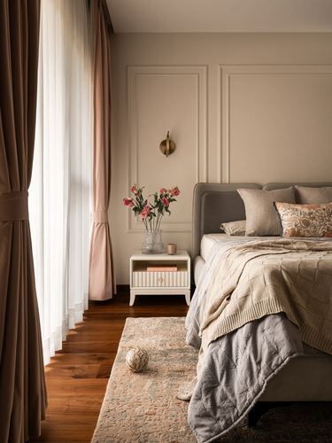 Beige bedroom with upholstered bed, wall paneling, brass sconce, and sheer pink curtains by window