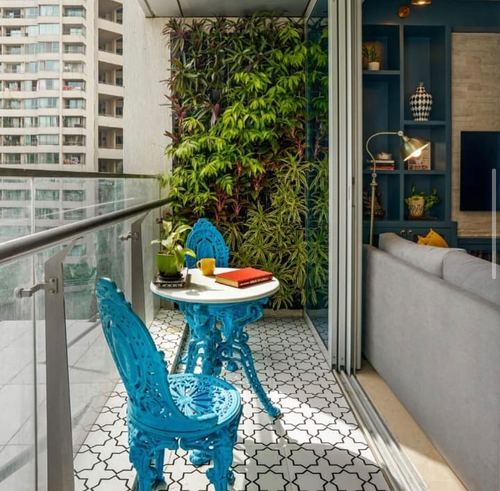 Blue cast-iron bistro set on patterned tile balcony against a living green wall, city view beyond