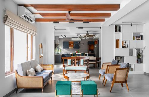 Open living room with cane furniture, teal ottomans, and wood beam ceiling leading to dining area