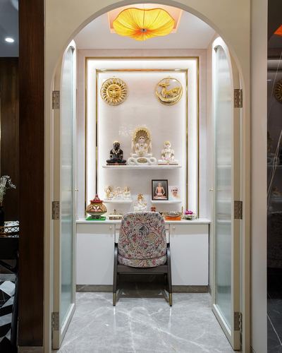 Arched pooja room with glass doors, gold niche, deity idols, and grey marble floor