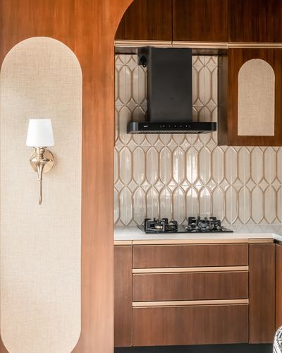 Wood-panelled kitchen corner with patterned tile backsplash, black chimney hood, and arched fabric niche with brass sconce
