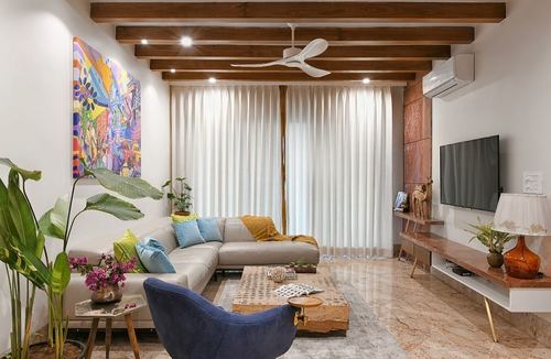 Living room with beige sectional, blue velvet chair, colorful artwork, and exposed wood beam ceiling
