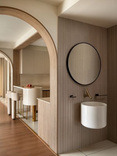 Arched wooden doorway leads to a beige-tiled bathroom with round mirror and wall-hung basin