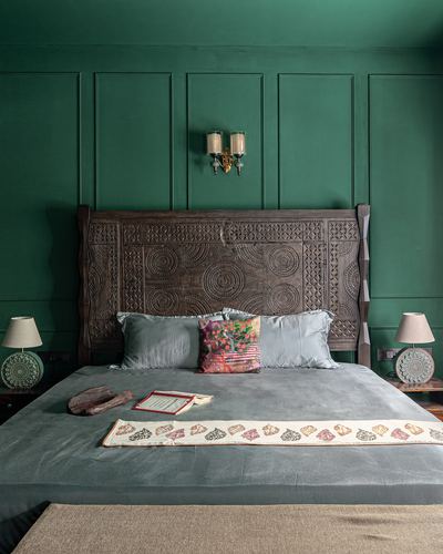 Carved wooden headboard against dark green panelled wall with block-print runner on grey bed