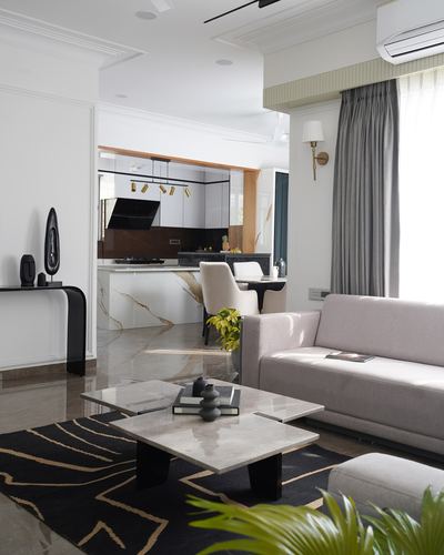 Living room with marble coffee table, grey sofa, black rug, opening into kitchen and dining beyond
