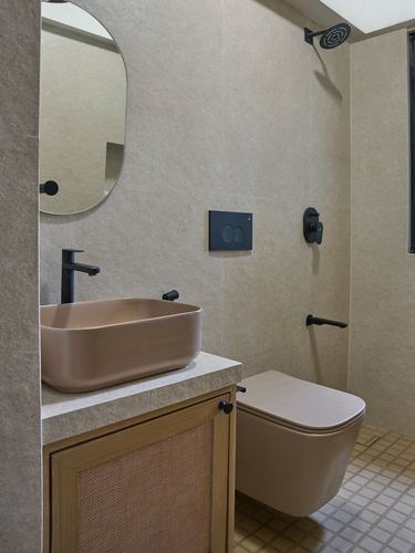 Bathroom with beige stone walls, blush vessel sink, wall-hung toilet, cane cabinet, and black fixtures