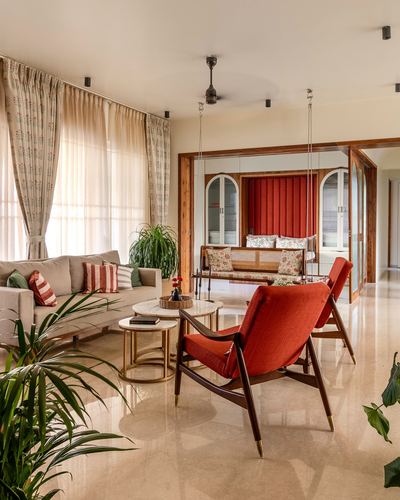 Living room with beige sofa, red mid-century chairs, marble coffee tables and a hanging cane swing beyond arched niches