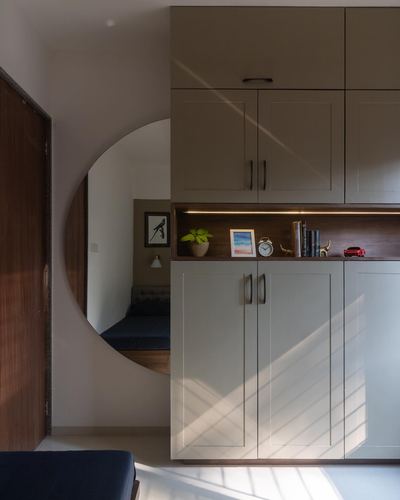 Sunlit foyer with circular wall mirror, wooden door, and built-in cabinetry with lit display niche