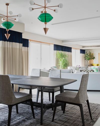 Dining table with grey chairs beneath green glass pendant lights, open living room beyond