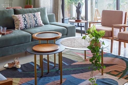Sage green sofa with patterned cushion beside layered round nesting tables on a geometric rug